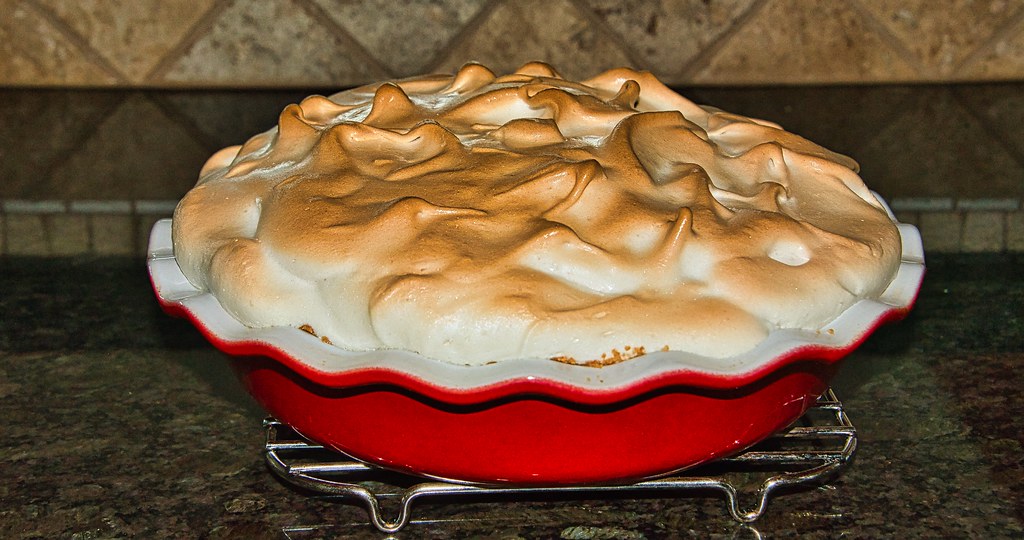 A golden-brown toasted meringue pie sits in a bright red scalloped dish on a metal cooling rack. — illustrating “A Bob Bob Ricard Birthday” on Florence and Mary