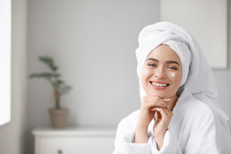 A smiling woman in a white bathrobe and dotted head towel has cream dots on her cheeks. — illustrating “Activbod Pick Me Up Scrub | Review” on Florence and Mary