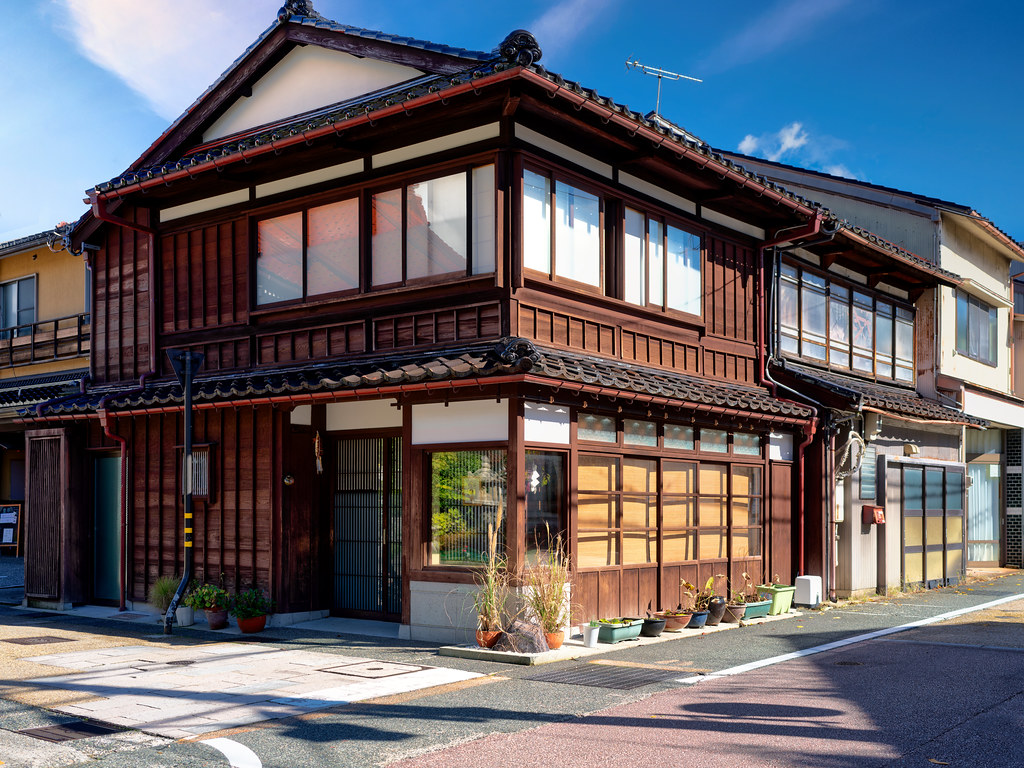 A traditional two-story dark wooden Japanese building with tiled roof sits on a sunny corner sidewalk. — illustrating “Afternoon Tea at Sketch” on Florence and Mary
