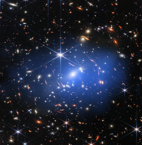 A deep-field space photo shows a hazy blue galaxy cluster with orange lensed arcs and spiked stars. — illustrating “All About Orange Collection from Mac” on Florence and Mary