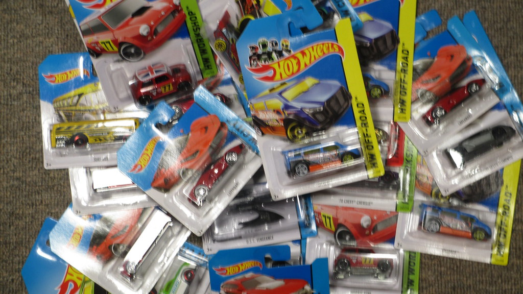 A scattered pile of packaged Hot Wheels toy cars in blue and yellow blister packs on gray carpet. — illustrating “April Favourites” on Florence and Mary