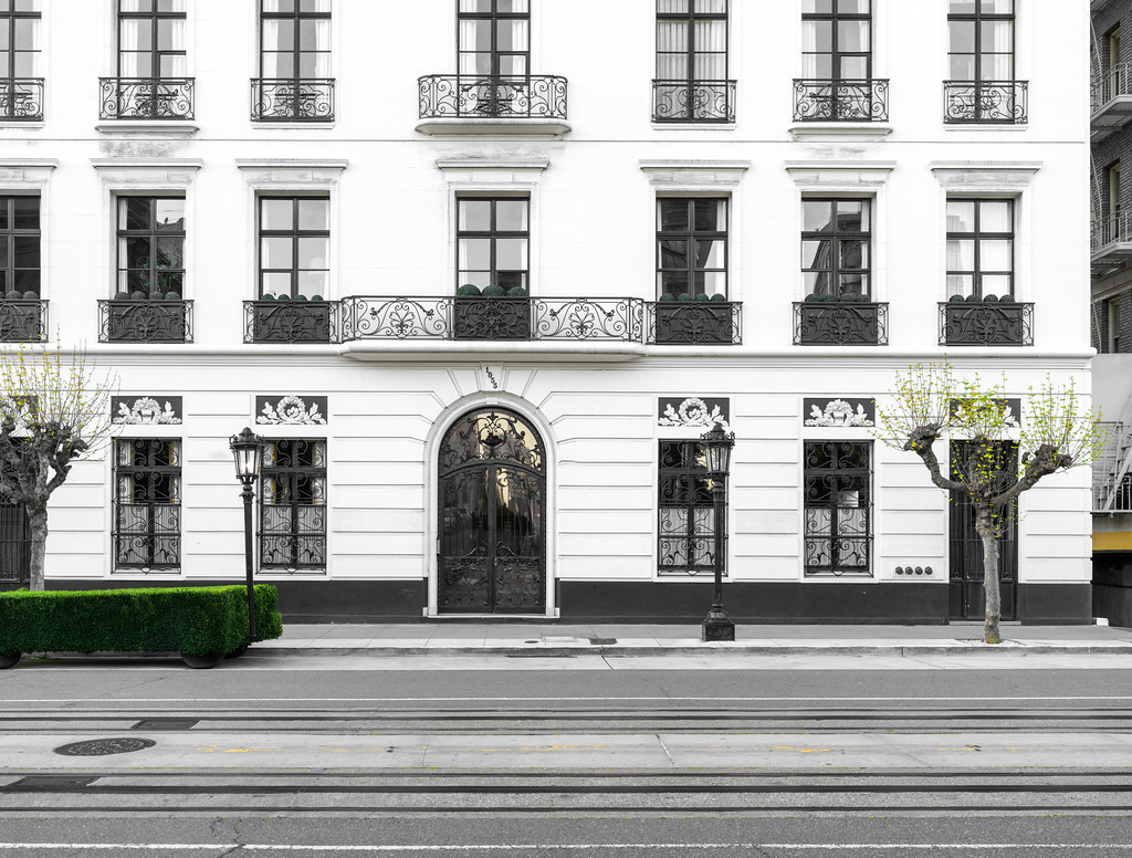 A white building facade with ornate black iron balconies and an arched gate behind green hedges. — illustrating “At Home Manicure with Scholl” on Florence and Mary