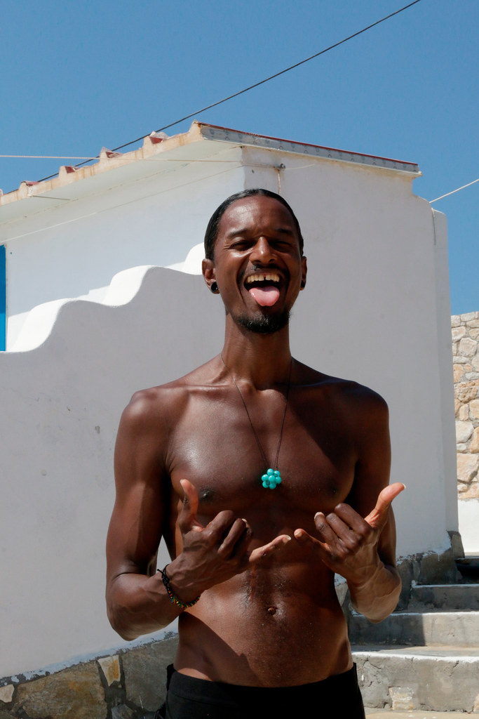 A shirtless laughing man with a turquoise necklace sticks out his tongue making shaka signs outdoors. — illustrating “Baby's Pearl & Swarovski Bracelet by Sugarpuss London” on Florence and Mary
