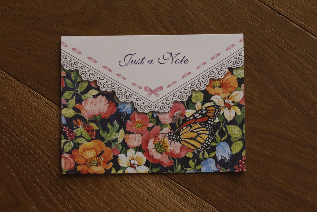 A Just a Note card with orange flowers and a monarch butterfly rests on a dark wooden surface. — illustrating “BDEM: My Typical Day – Part 2” on Florence and Mary