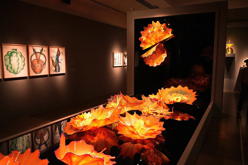 Amber rippled glass sculptures glow on a reflective black surface in a dimly lit art gallery. — illustrating “Beauty Empties June 2015” on Florence and Mary