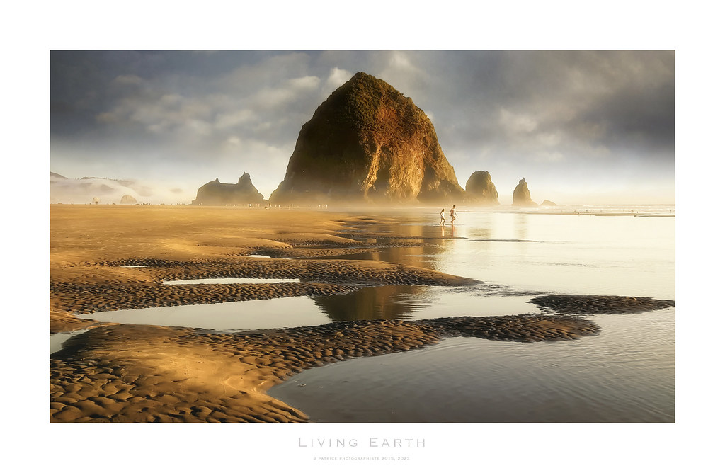 A large sea stack towers over a wide sandy beach at golden hour with tide pools and two distant figures. — illustrating “Beauty Empties | May 2015” on Florence and Mary