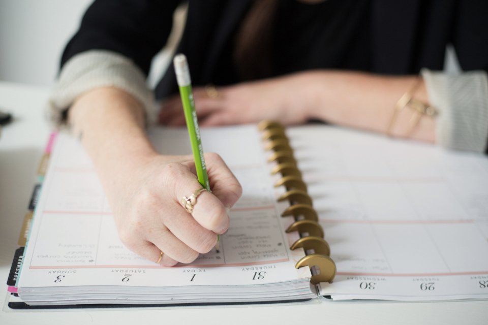 A hand with gold rings writes in a gold disc-bound planner using a bright green pencil on a white desk. — illustrating “BEDM: Spring is here” on Florence and Mary