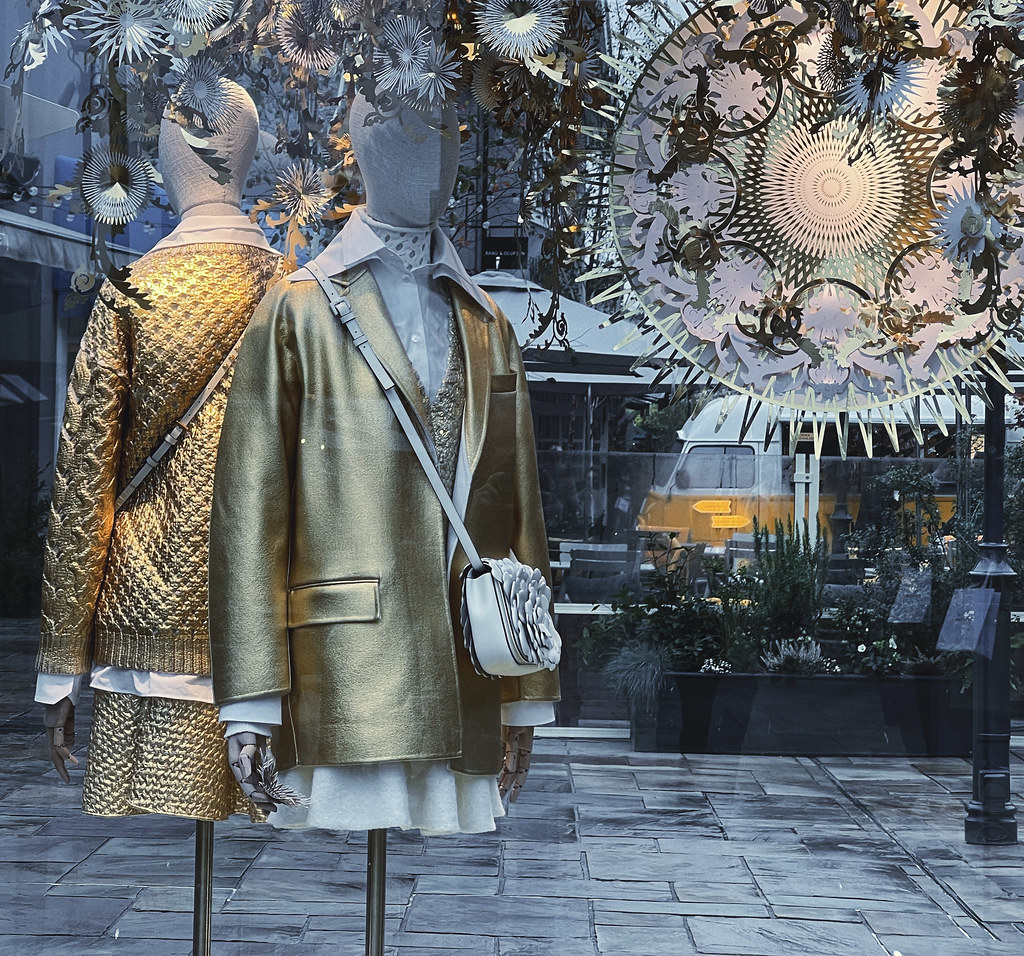 A store window display shows two mannequins in shimmering metallic gold jackets and skirts with white shirts. — illustrating “Bicester Village Shopping Review” on Florence and Mary