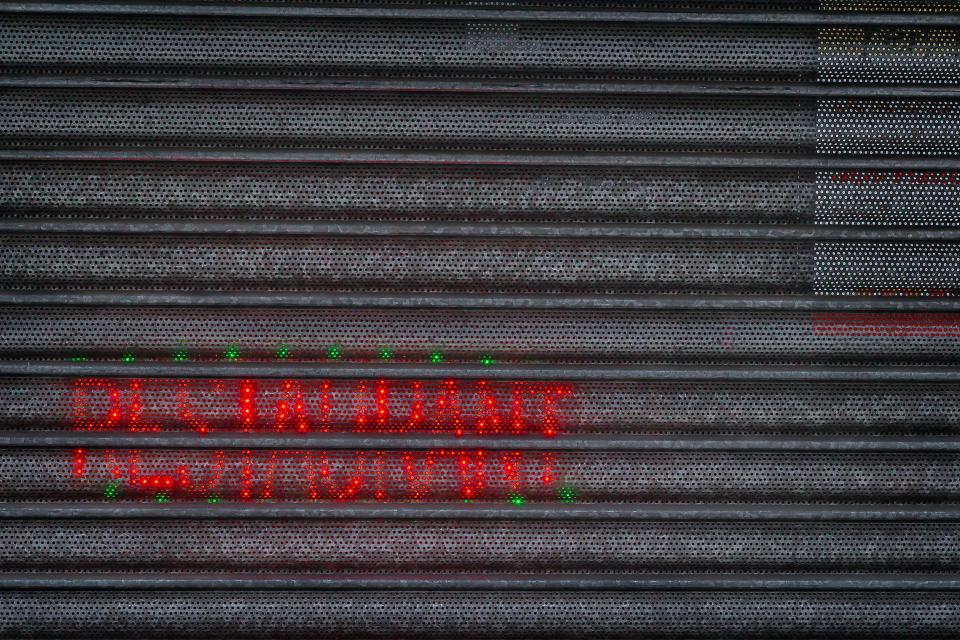 A closed perforated metal security shutter shows red and green neon lights glowing through at night. — illustrating “Breakfast at Fortnum & Mason” on Florence and Mary