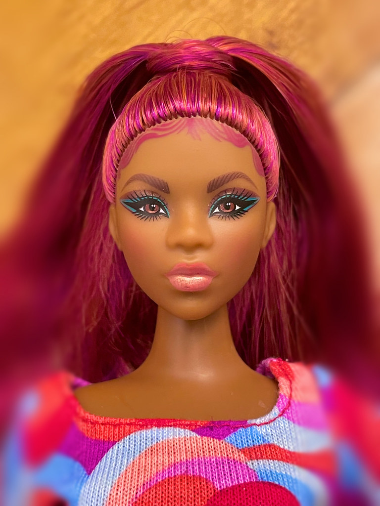 A close-up of a dark-skinned doll with vibrant magenta hair, turquoise eye makeup, and a wavy-patterned top. — illustrating “Chanel Illusion D'Ombre Long Wear Luminious Eyeshadow in Fa…” on Florence and Mary