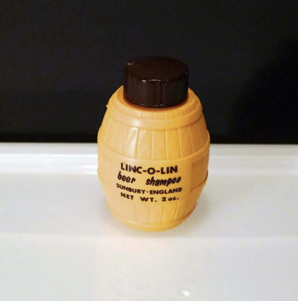 A small orange barrel-shaped bottle of beer shampoo with a dark brown cap sits on a white surface. — illustrating “Clinque 7 day scrub cream review” on Florence and Mary