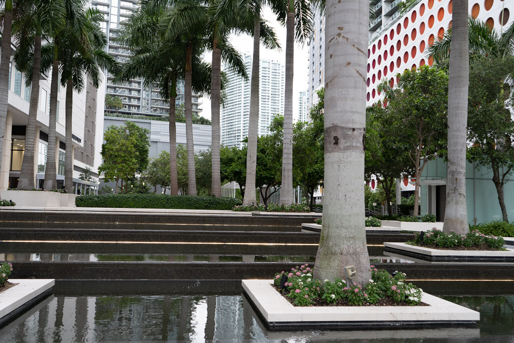 A modern plaza features tiered reflective pools, palm trees in white planters, and skyscrapers with orange circles. — illustrating “Day Designer Review & A Paperchase Dupe” on Florence and Mary