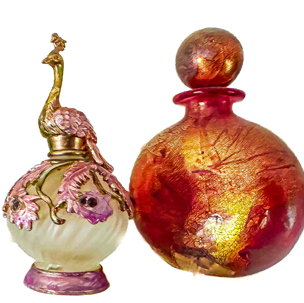 Two ornate perfume bottles include a golden peacock stopper and a mottled red-and-gold spherical vessel. — illustrating “DIPTYQUE; Eau Moheli Eau De Toilette Roll-On” on Florence and Mary