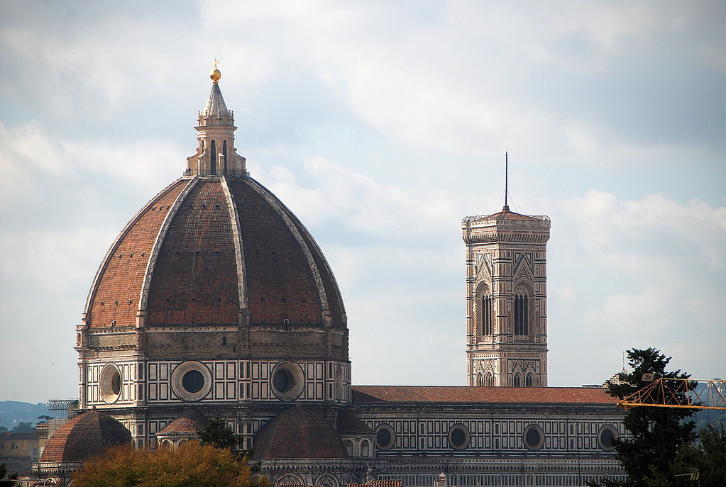 A large reddish-brown cathedral dome and marble bell tower rise above autumn trees against a cloudy sky. — illustrating “Florence and Mary | A New Look” on Florence and Mary