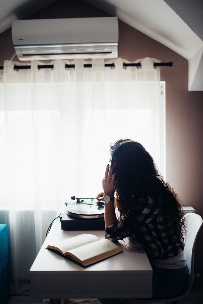 A woman with long curly hair and headphones sits at a white desk with a record player by a bright window. — illustrating “From Desk to Disco | Mistletoe Ready” on Florence and Mary