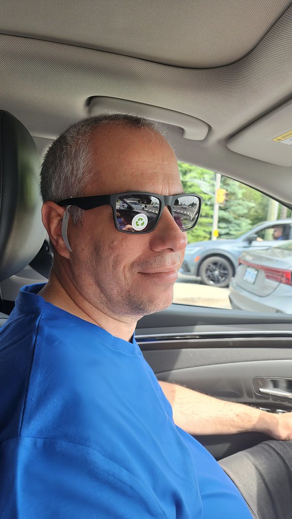 A man in a blue shirt and sunglasses with a recycling sticker sits smiling in a car passenger seat. — illustrating “Ham Holy Burger | London” on Florence and Mary