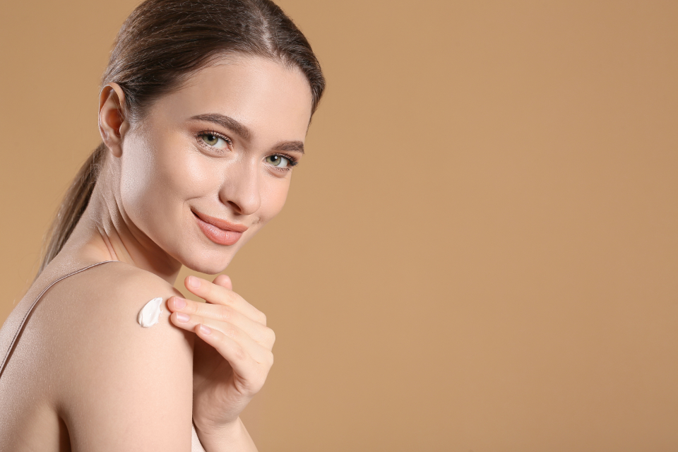 A smiling woman with brown hair pulled back has white cream on her shoulder against a beige backdrop. — illustrating “In Flight Skincare Kit from Heaven Skincare” on Florence and Mary