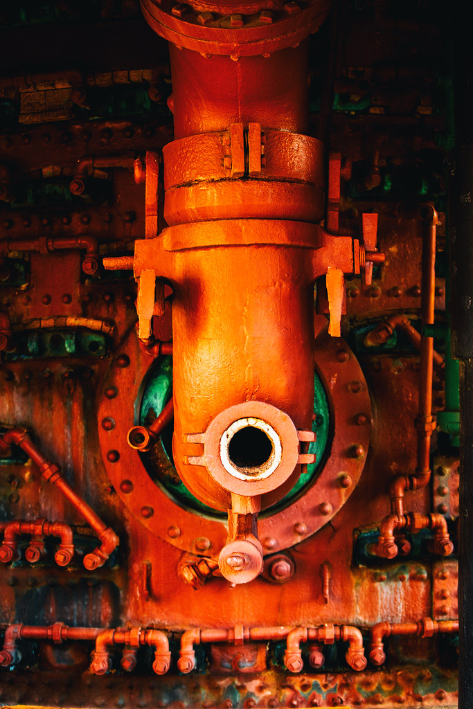Weathered industrial pipes and valves coated in vibrant reddish-orange paint fill a close-up machinery view. — illustrating “It's Not You It's Me” on Florence and Mary