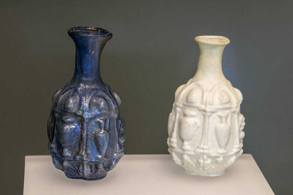 Two antique mold-blown glass bottles in cobalt blue and creamy white sit on a white museum shelf. — illustrating “Jo Malone Ginger Biscuit Cologne” on Florence and Mary