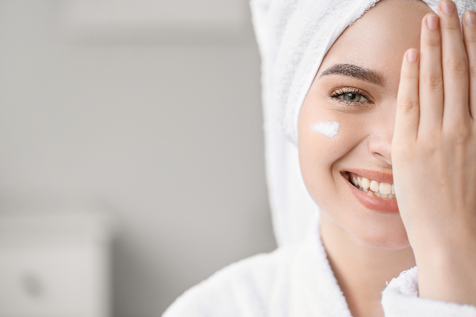 A smiling woman in a white head towel covers one eye, showing a dab of white cream on her cheek. — illustrating “Kiehls Skincare Regime” on Florence and Mary