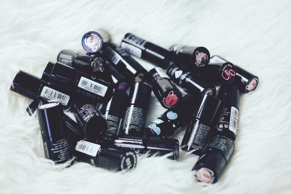 Black cylindrical makeup containers with barcodes and colorful shade labels scatter across a white faux fur surface. — illustrating “Limited Edition Vaseline Paint The Town Lip Therapy in Spic…” on Florence and Mary