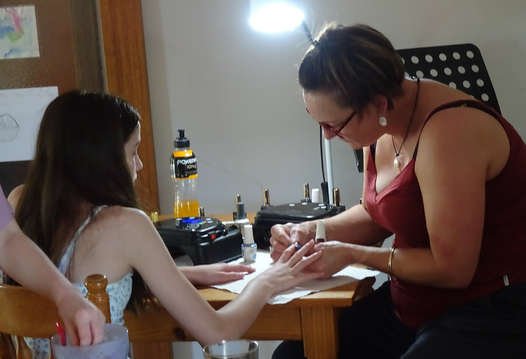 A woman in a red tank top carefully applies nail polish to a young girl fingers at a wooden table. — illustrating “Liz Earle Cleanse & Polish Hot Cloth Cleanser” on Florence and Mary