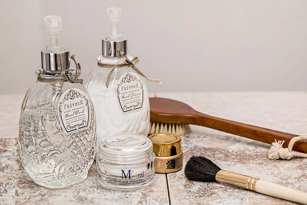 Ornate glass soap dispensers, cream jars, a makeup brush, and a wooden bath brush sit on light marble. — illustrating “L'Oreal Vs Garnier Micellar Water Battle” on Florence and Mary