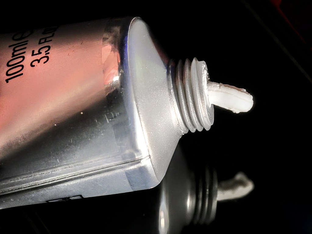 A silver metallic tube squeezes thick white cream onto a glossy black surface showing a clear reflection. — illustrating “Lotil Original Cream Review” on Florence and Mary