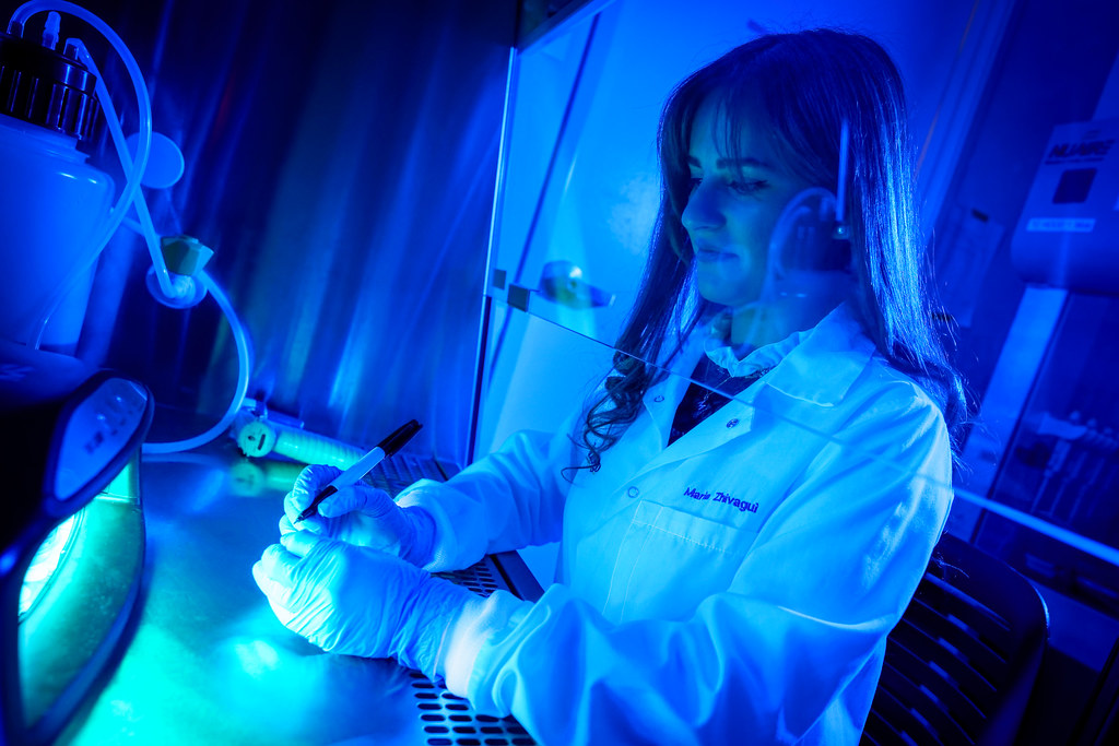 A female scientist in a white coat and gloves writes with a marker inside a blue-lit lab workstation. — illustrating “MAC Dark Angel Nail Lacquer Review” on Florence and Mary