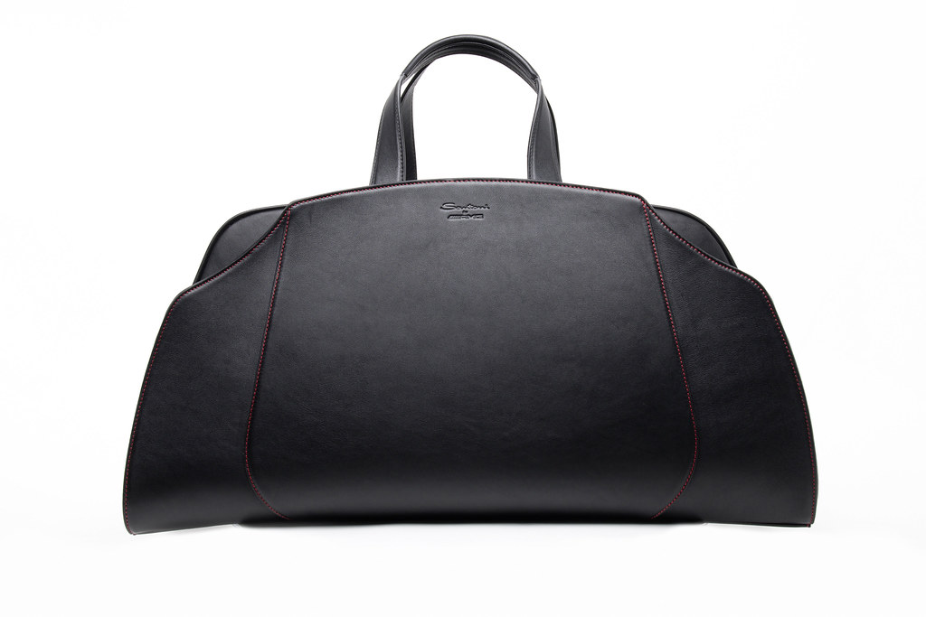A large black leather bag with a curved silhouette, red contrast stitching, and top handles sits on white. — illustrating “Mac Osbourne Collection Purchases & swatches” on Florence and Mary