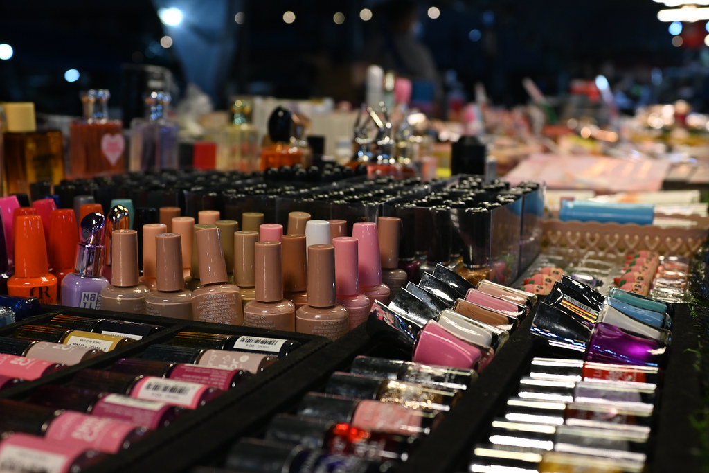 Colorful nail polish bottles and perfume containers pack a brightly lit night market stall display densely. — illustrating “Maybelline Colour Show Brocades // Rosy Rosettes Review” on Florence and Mary