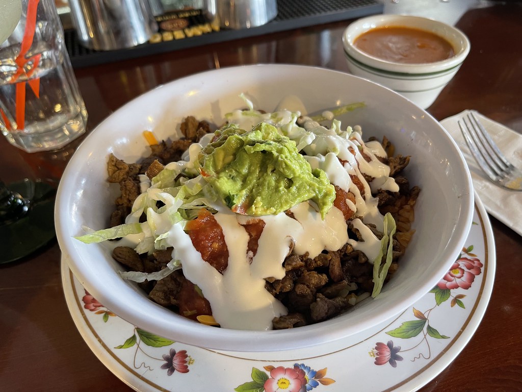 A white bowl of shredded beef, lettuce, salsa, sour cream, and guacamole sits on a floral restaurant plate. — illustrating “Miller & Carter Steak Night, Epping Essex” on Florence and Mary