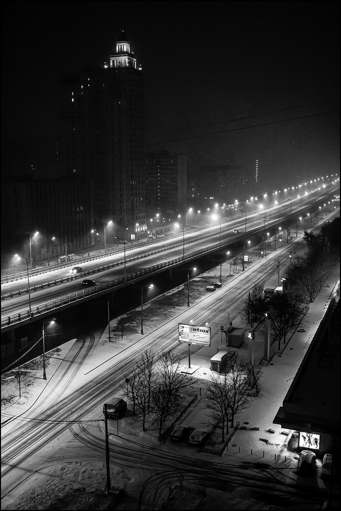 A black-and-white aerial night view shows a snowy city highway lined with bright streetlights and lit buildings. — illustrating “My Everyday Face” on Florence and Mary