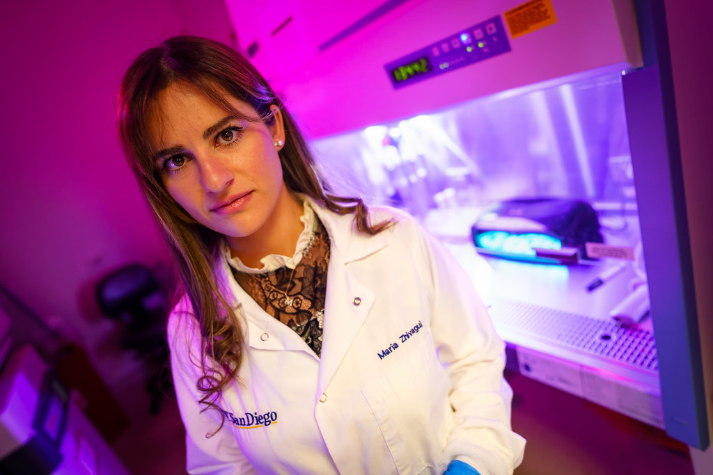 Woman in a white lab coat stands in a laboratory lit by bright purple and pink light. — illustrating “Nails Inc Modern Art Accent Nail” on Florence and Mary