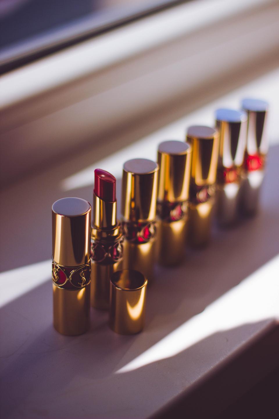 Gold lipstick tubes with ornate circular logos line a white ledge, one open berry-red bullet. — illustrating “Molton Brown Nearly Nude Lipstick” on Florence and Mary