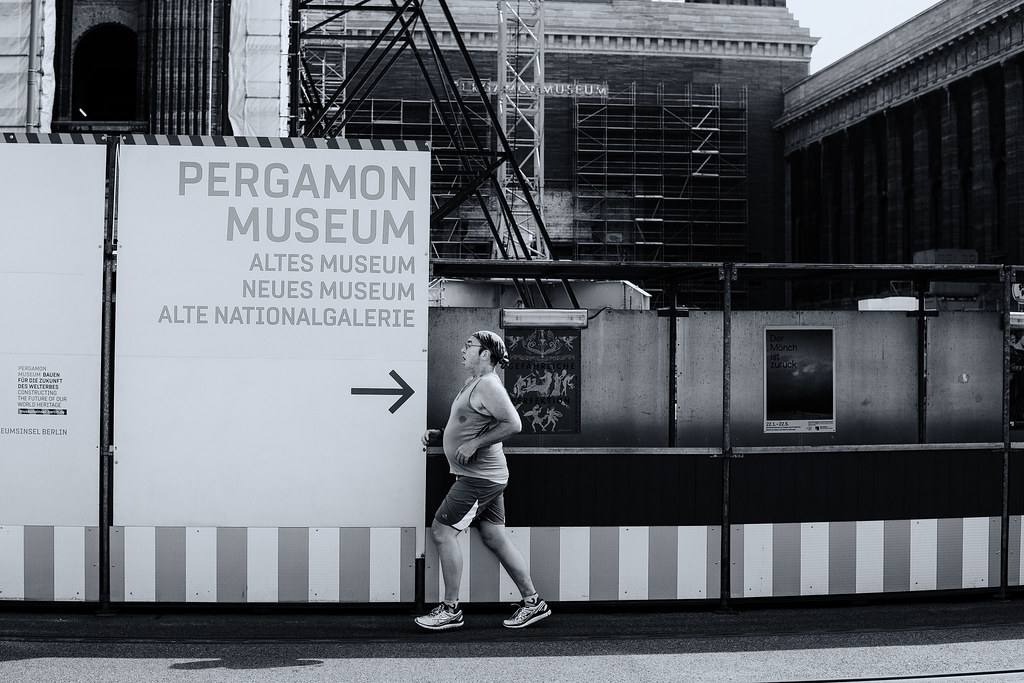 Black-and-white photo of a man with a headband jogging past Pergamon Museum construction fencing. — illustrating “NEW Collection Contour Kit” on Florence and Mary