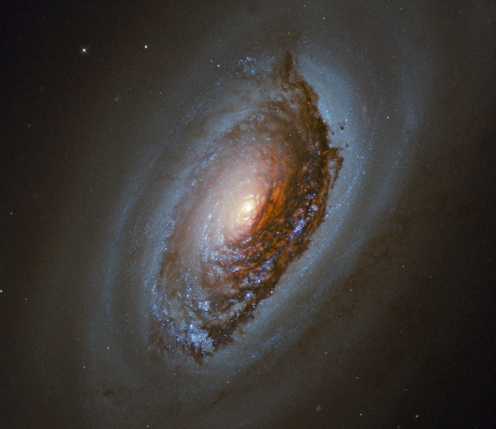Spiral galaxy with a bright core and thick dark brown dust lanes against starry black space. — illustrating “New Year, New Hair” on Florence and Mary