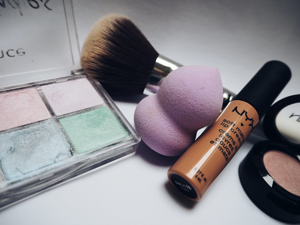 Pastel color-correcting palette, purple sponge, makeup brush, and NYX lip cream tube arranged together. — illustrating “NYX Make Up” on Florence and Mary