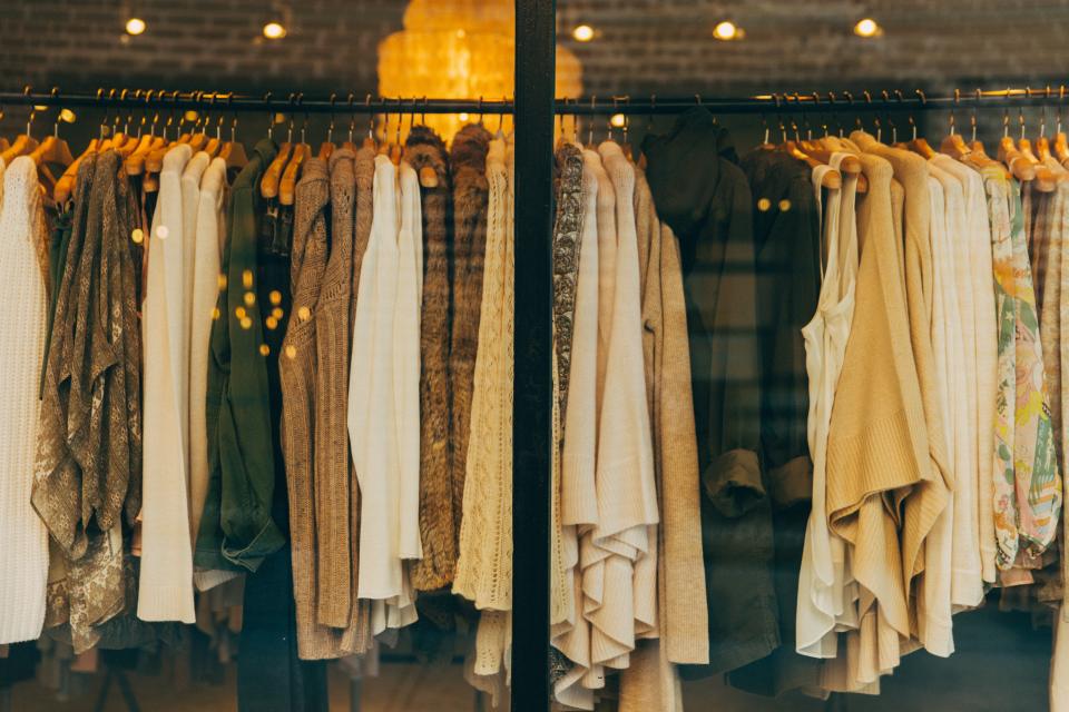 Neutral sweaters and shirts hang on wooden hangers in a boutique window with warm reflected lights. — illustrating “OOTD: Converse Casual” on Florence and Mary