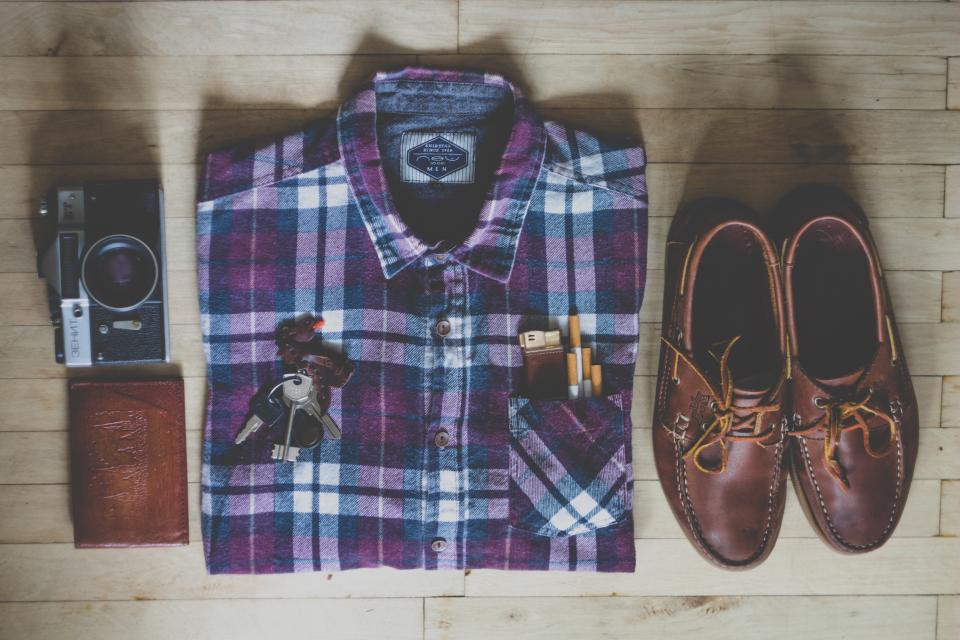 Flat lay with purple plaid shirt, brown boat shoes, vintage camera, and leather wallet on wood. — illustrating “OOTD - Ode to Margaret Thatcher” on Florence and Mary
