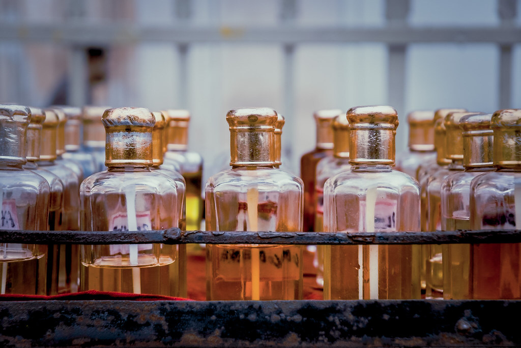 Rows of small glass vials with metallic gold caps and yellowish liquid in a rusty metal tray. — illustrating “Paco Rabanne Lady Million Review” on Florence and Mary