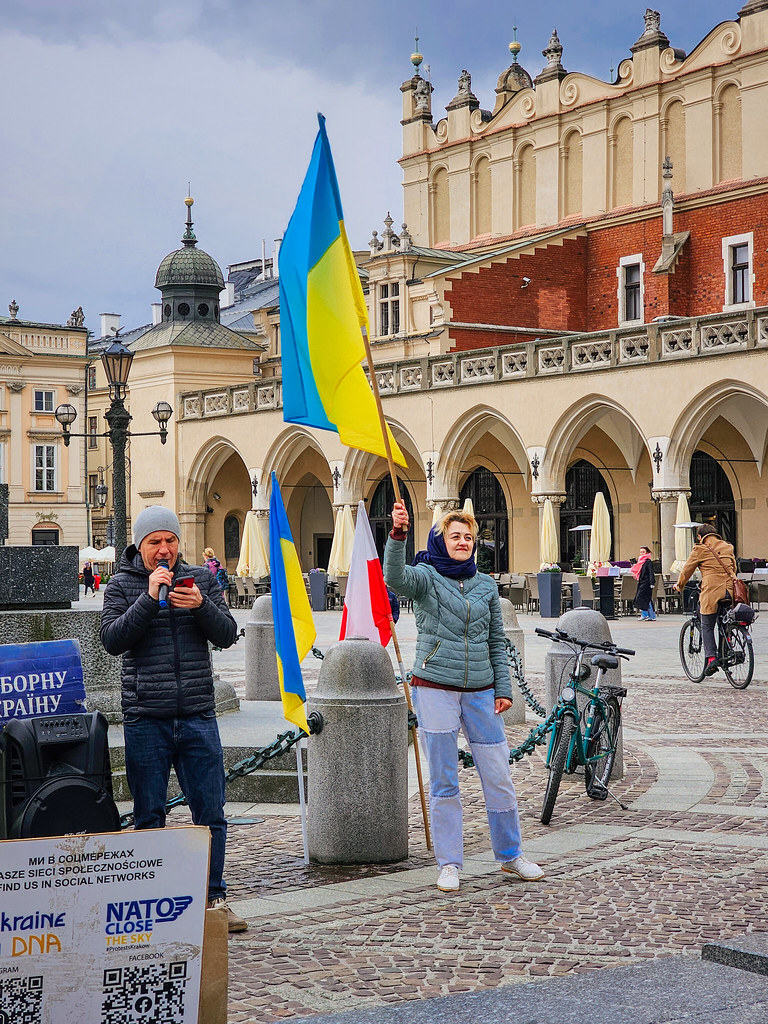 Woman holds a large Ukrainian flag in a historic square beside a man with a microphone. — illustrating “Pay Day Beauty Haul & Repurchases | Part 2” on Florence and Mary