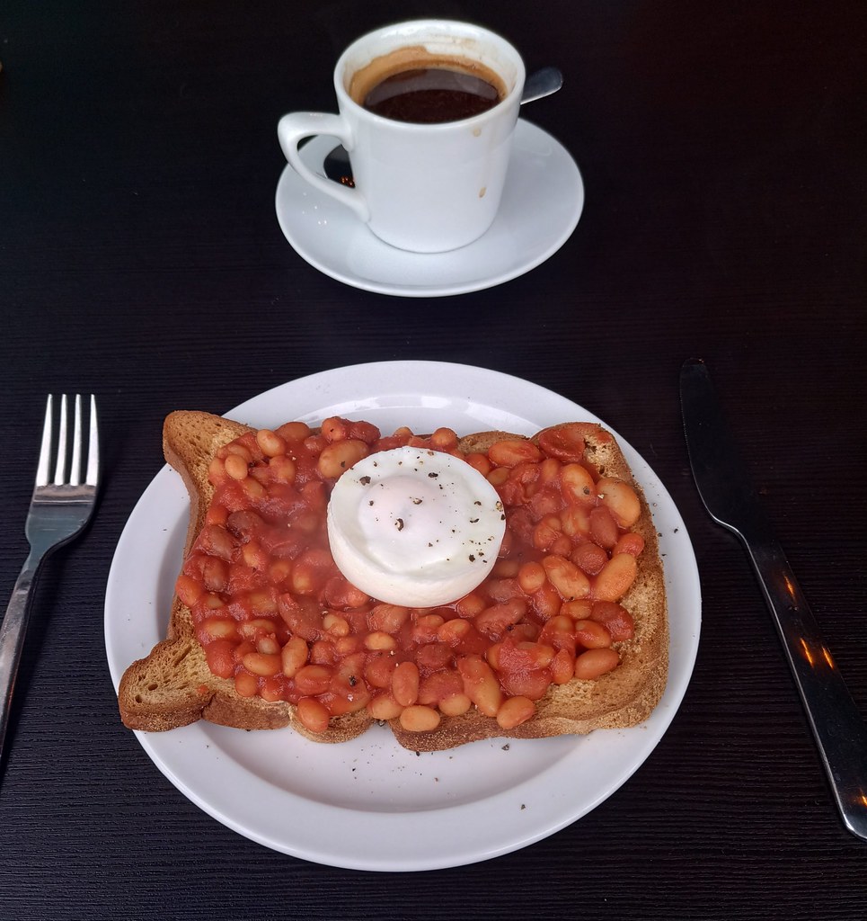 Baked beans on thick toast topped with a poached egg, served with black coffee on dark table. — illustrating “Perfectly Poached Eggs” on Florence and Mary