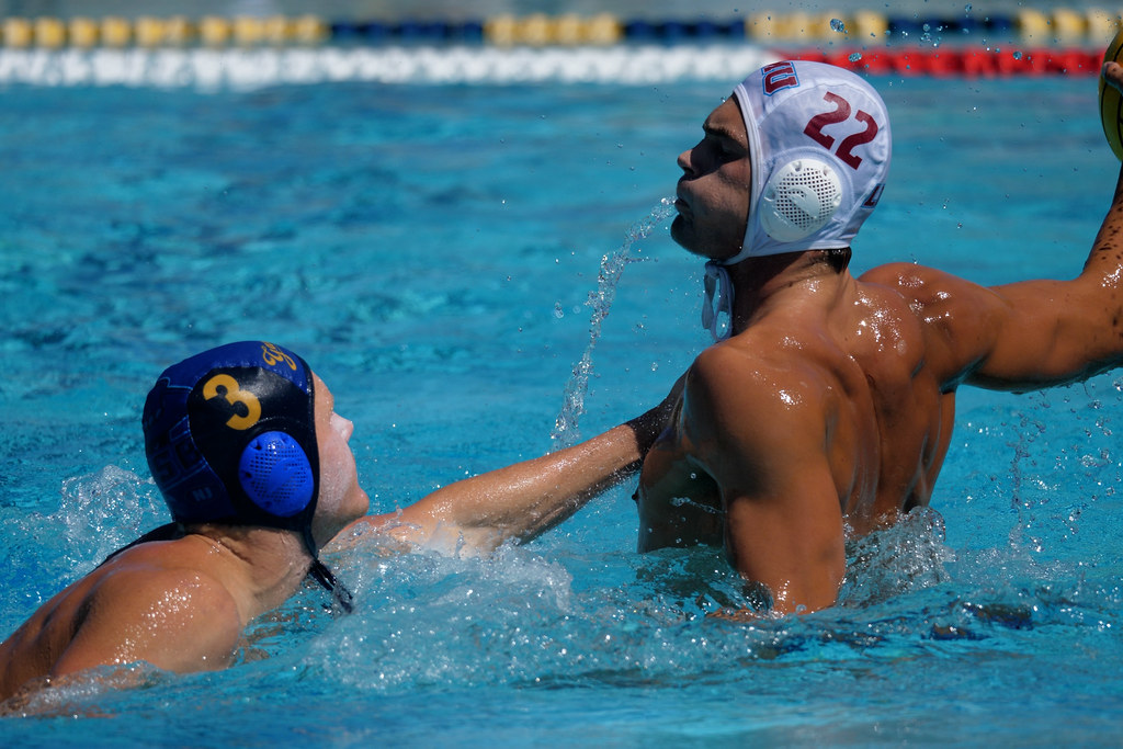 Two water polo players compete in a blue pool, one in white cap numbered twenty-two splashing. — illustrating “Preparing for Santa….” on Florence and Mary
