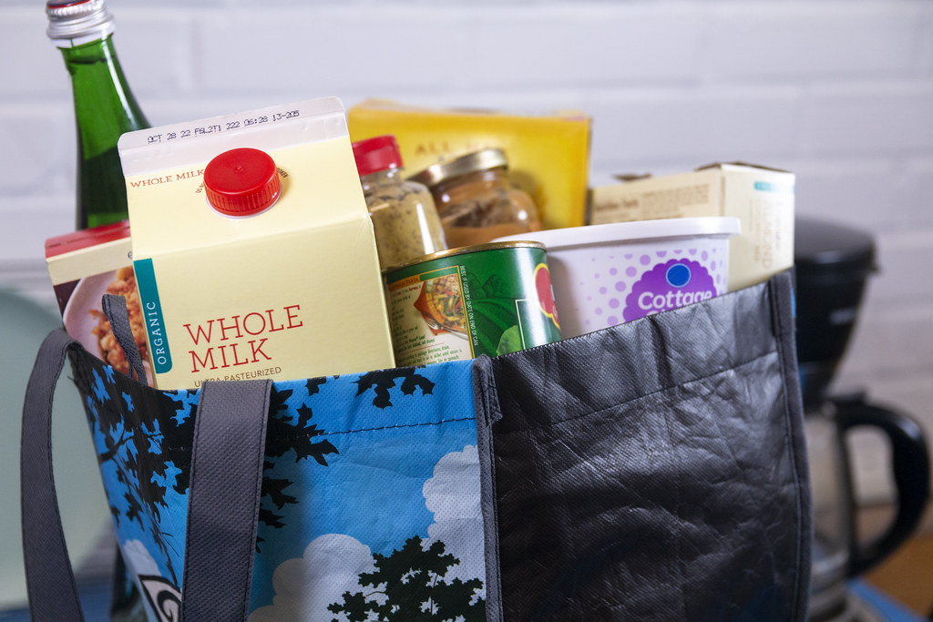 Blue patterned reusable bag filled with groceries including milk and cottage cheese by white brick. — illustrating “Repurchases Haul” on Florence and Mary