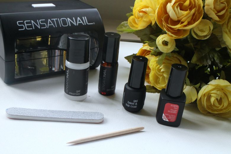 Black LED nail lamp and four gel polish bottles arranged with tools and yellow roses. — illustrating “Sensationail Nail Starter Kit Review” on Florence and Mary