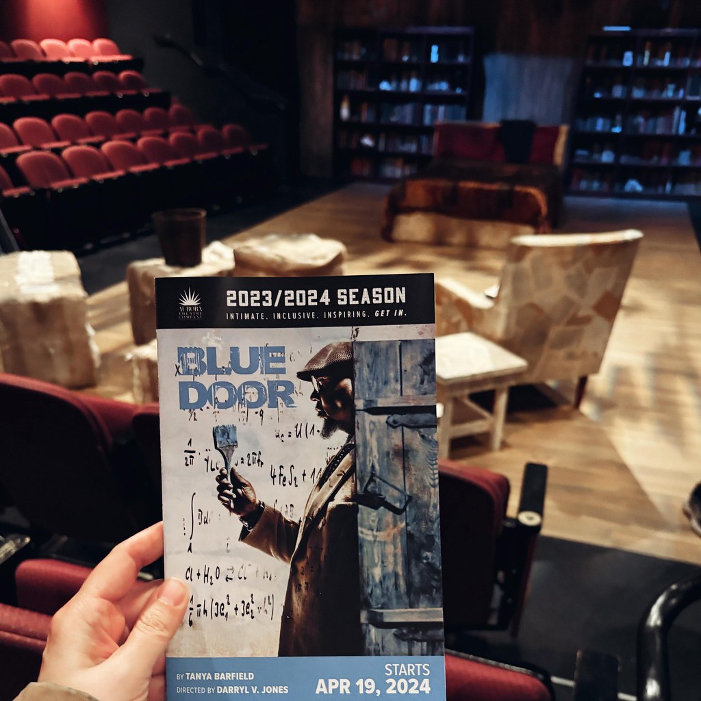 Hand holds a Blue Door theater program in a dim auditorium with red seats and furnished stage. — illustrating “September Empties” on Florence and Mary