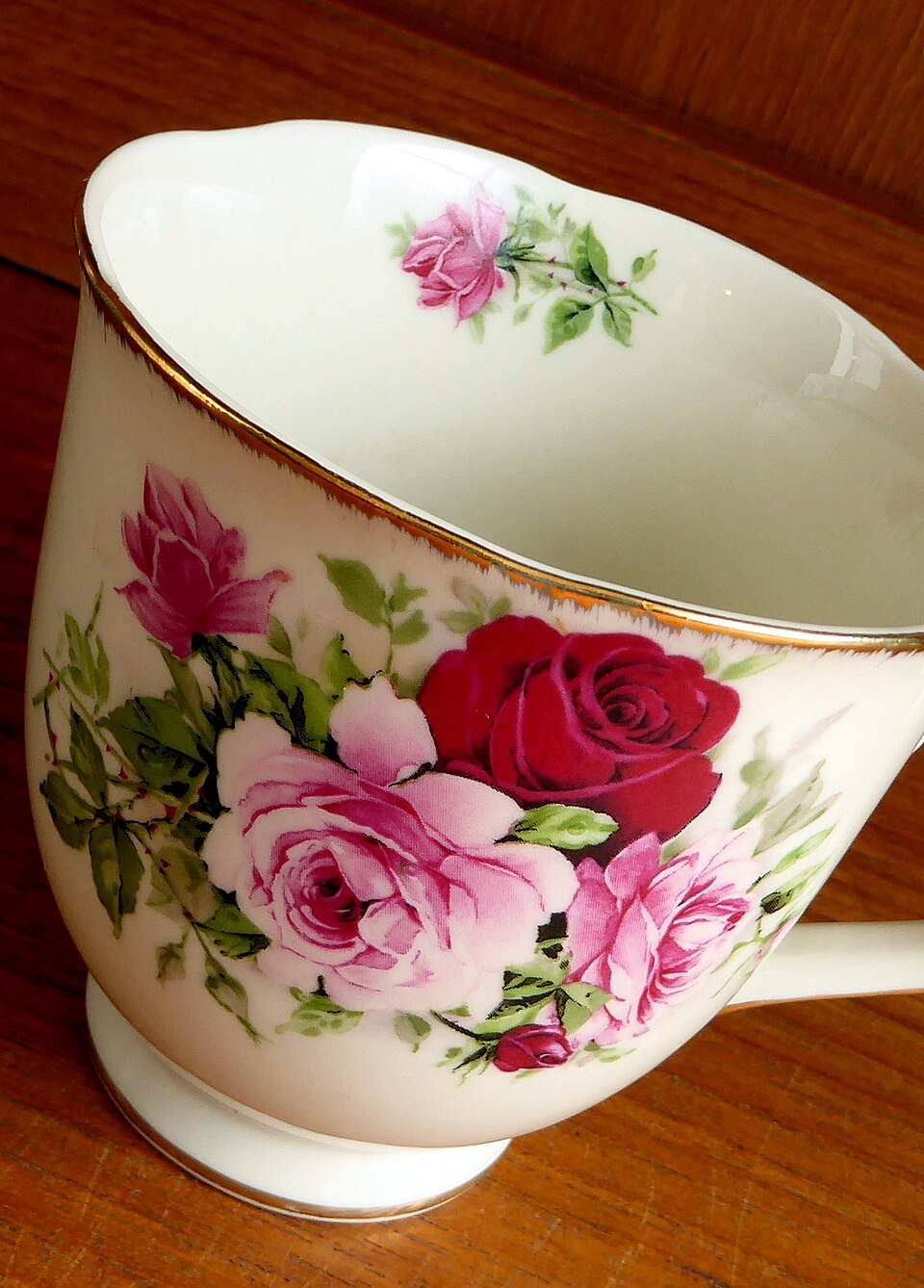 White porcelain teacup decorated with pink and red roses and a gold rim on wooden surface. — illustrating “Sick Day Saviours” on Florence and Mary