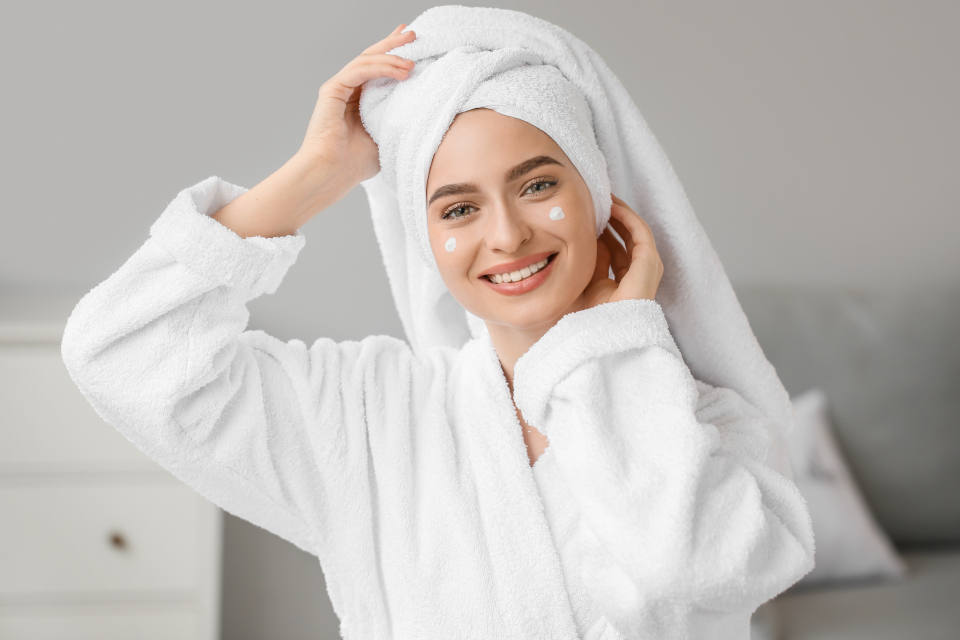 Smiling young woman in white plush bathrobe and head towel with cream dots on her cheeks. — illustrating “St Ives Invigorating Apricot Body Scrub” on Florence and Mary