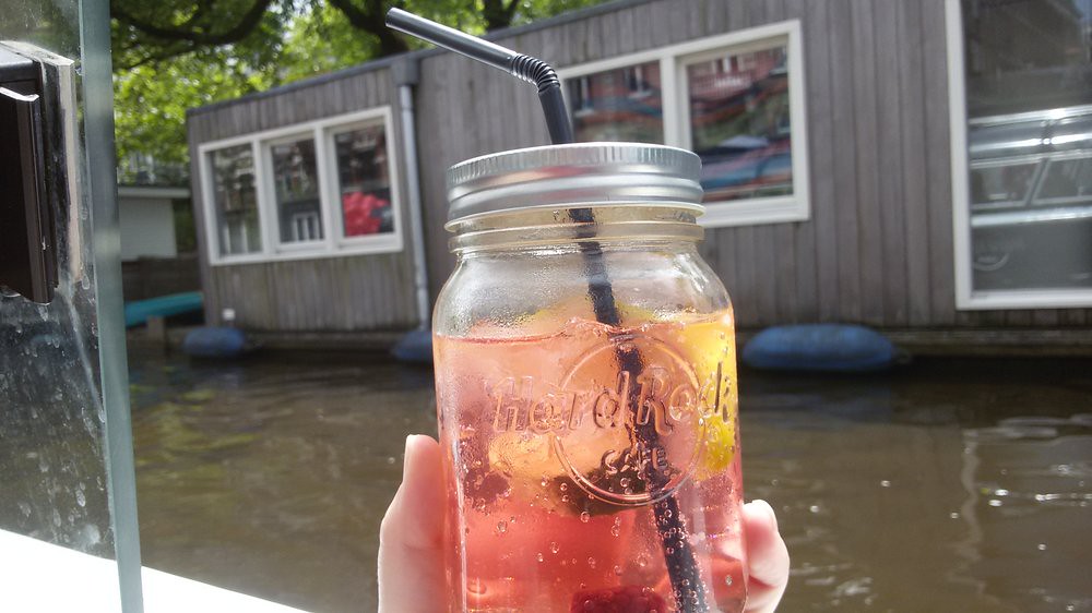 Hand holds Hard Rock Cafe mason jar of pink fizzy drink with citrus beside a canal. — illustrating “Sunday Spend: Gold Scratch Ring from NEXT” on Florence and Mary